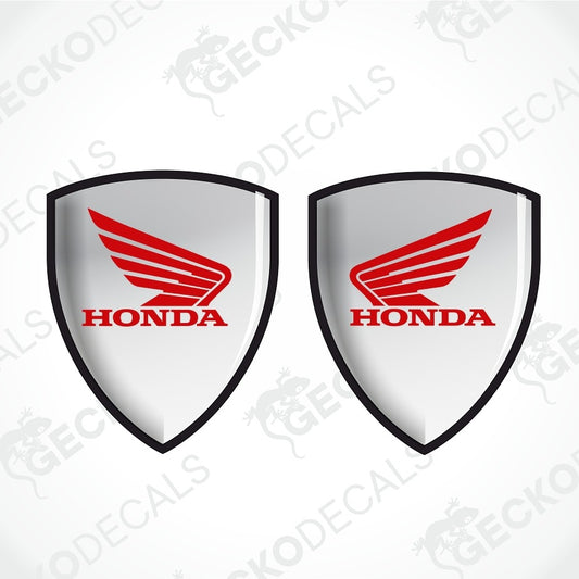 Two identical Honda shield-shaped decals on a light gray background with diagonal watermark text. Each decal has a silver-gray center, a red Honda wing logo, and red HONDA text outlined in black.