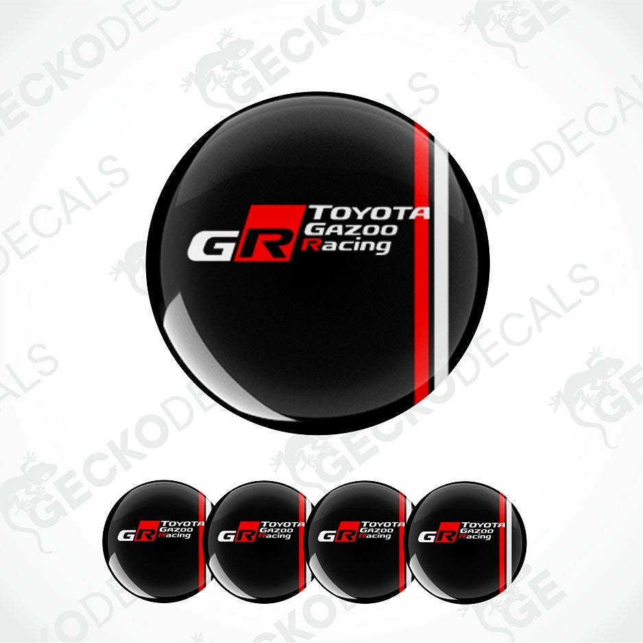 A glossy black oval decal or badge featuring the Toyota Gazoo Racing GR logo, shown with four smaller identical decals along the bottom on a light gray background with faint watermark text.