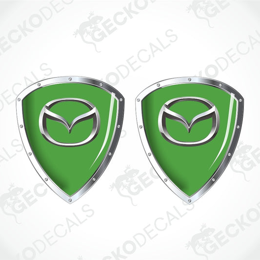 Two green shield-shaped decal designs with silver metallic borders and a silver Mazda logo in the center, shown on a light gray background with repeated GECKODECAL watermarks.