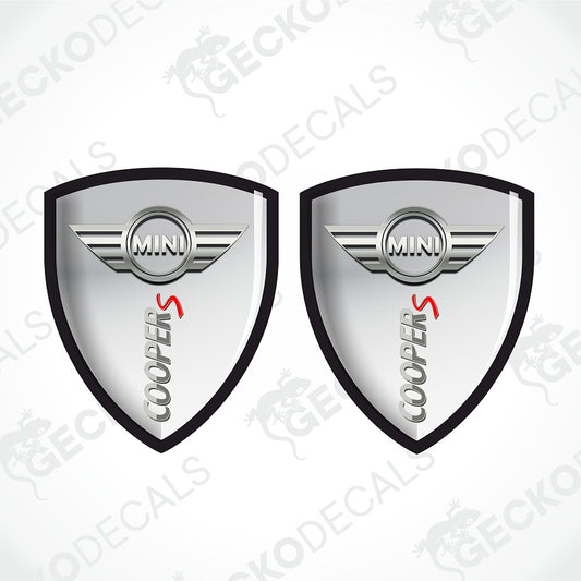 Two identical silver and black Mini Cooper S shield-shaped decals on a light gray background with diagonal watermarks.