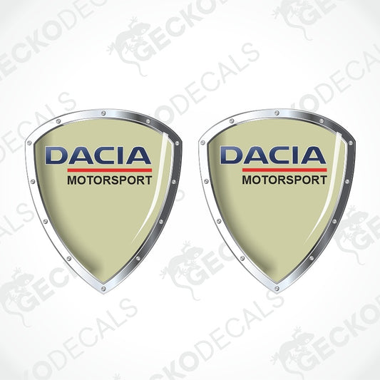 Two identical Dacia Motorsport shield-shaped decals on a white background with diagonal watermarks. The decals feature a light mint green center, silver metallic borders, and the Dacia Motorsport logo in blue and red.