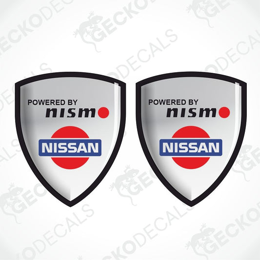 Two identical shield-shaped decals featuring the 'Powered by Nismo' and 'Nissan' logo, displayed side-by-side on a light gray background with diagonal watermarks.