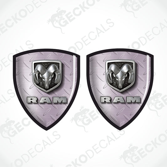Two matching Ram shield-shaped decals on a white background, each featuring a silver ram head emblem above the word RAM in metallic lettering, with a light lavender-gray diamond plate texture and black border.