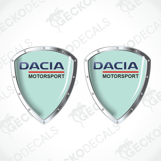 Two identical Dacia Motorsport shield-shaped decals on a white background with diagonal watermarks. The decals feature a light mint green center, silver metallic borders, and the Dacia Motorsport logo in blue and red.