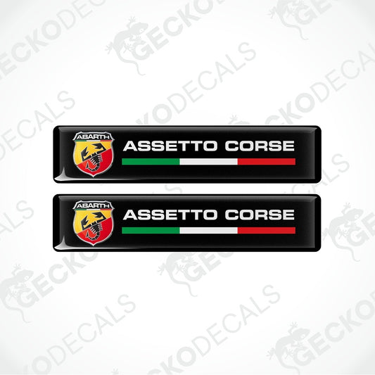 Two black rectangular Abarth Assetto Corse decals with the Abarth logo, white text, and green, white, and red stripes, shown on a light gray background with faint Geekodec watermarks.