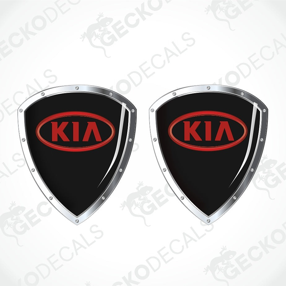 Two black shield-shaped Kia decal stickers with silver borders and red oval Kia logos, shown on a light gray background with faint watermarks.