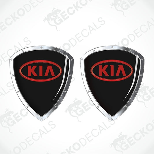 Two black shield-shaped Kia decal stickers with silver borders and red oval Kia logos, shown on a light gray background with faint watermarks.