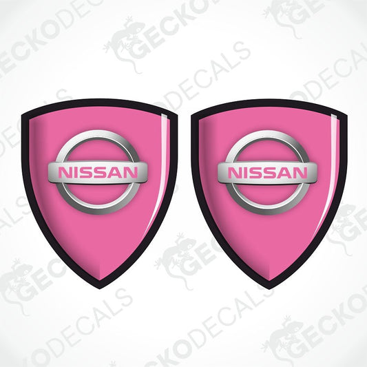 Two pink Nissan shield-shaped decals with the silver and pink Nissan logo in the center, shown on a white background with a faint watermark pattern.