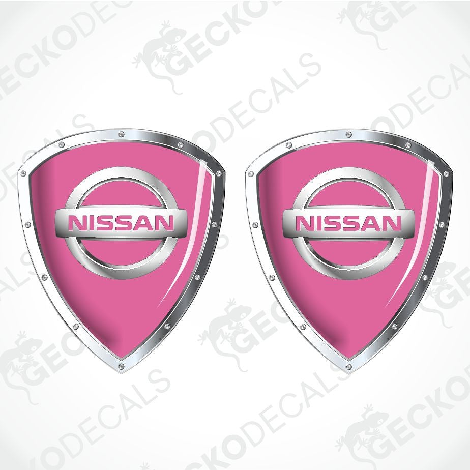Two pink Nissan shield-shaped decals with silver metallic borders and the Nissan logo in the center, shown on a light gray background with faint GECKODECS watermarks.