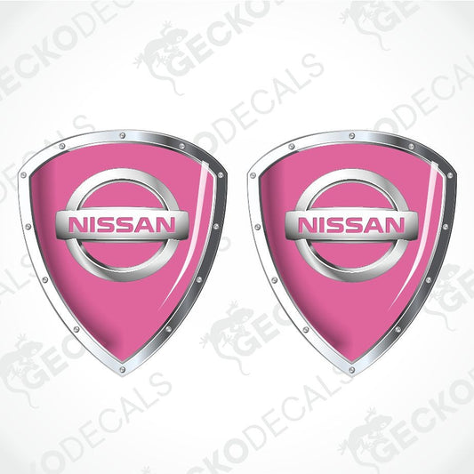 Two pink Nissan shield-shaped decals with silver metallic borders and the Nissan logo in the center, shown on a light gray background with faint GECKODECS watermarks.