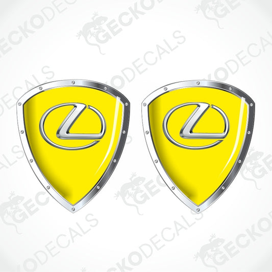 Two identical yellow shield-shaped decals with silver metallic borders and the Lexus logo in the center, shown on a white background with faint GECKODECALS watermarks.