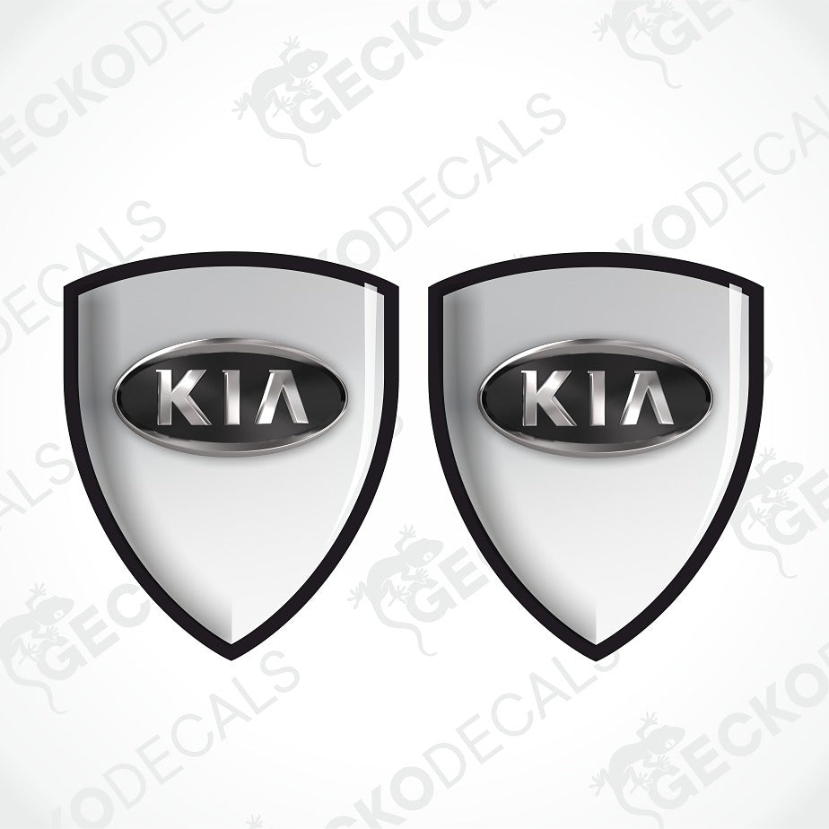 Two identical shield-shaped Kia decal designs on a light gray background with repeated GECKODECALS watermarks. Each shield has a black border, a silver oval center, and the word KIA in silver.
