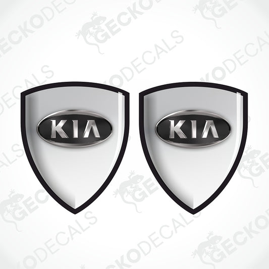 Two identical shield-shaped Kia decal designs on a light gray background with repeated GECKODECALS watermarks. Each shield has a black border, a silver oval center, and the word KIA in silver.