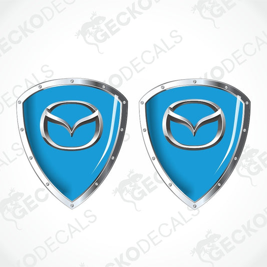 Two identical blue and silver Mazda shield-shaped decal designs shown side by side on a light gray background with faint diagonal watermark text.