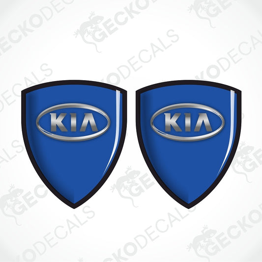 Two blue shield-shaped Kia decal stickers with silver oval logos and black outlines, shown on a white background with diagonal watermarks.
