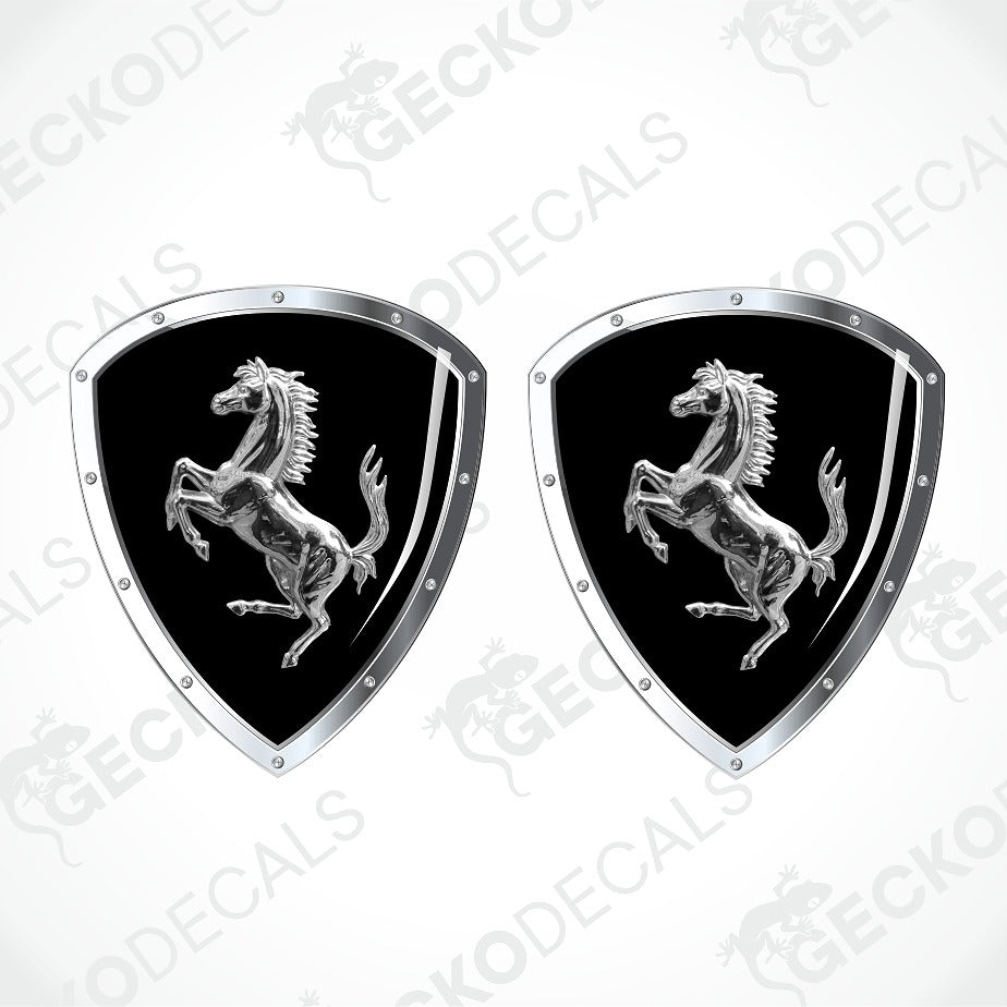 Two identical Ferrari shield-shaped decals on a light gray background with diagonal watermarks. Each decal has a black center with the silver prancing horse logo and a silver border with small rivet details.