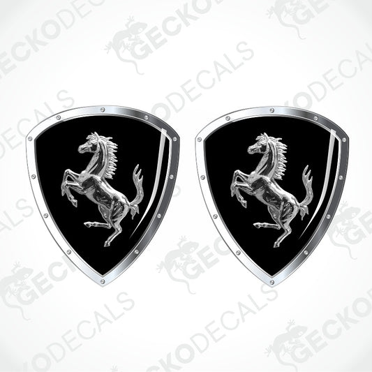 Two identical Ferrari shield-shaped decals on a light gray background with diagonal watermarks. Each decal has a black center with the silver prancing horse logo and a silver border with small rivet details.