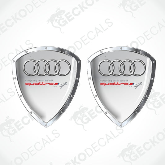 Two silver shield-shaped Audi quattro decal stickers on a white background with diagonal watermarks.