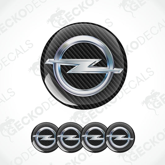 A set of circular car decals featuring the Opel logo, shown on a white background with a diagonal watermark pattern. The main decal at the top has a glossy black carbon fiber texture background with a silver metallic ring and logo, while the bottom row shows four smaller variants of the same decal.