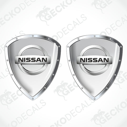 Two silver Nissan shield-shaped decal designs on a light gray background with diagonal watermark text.