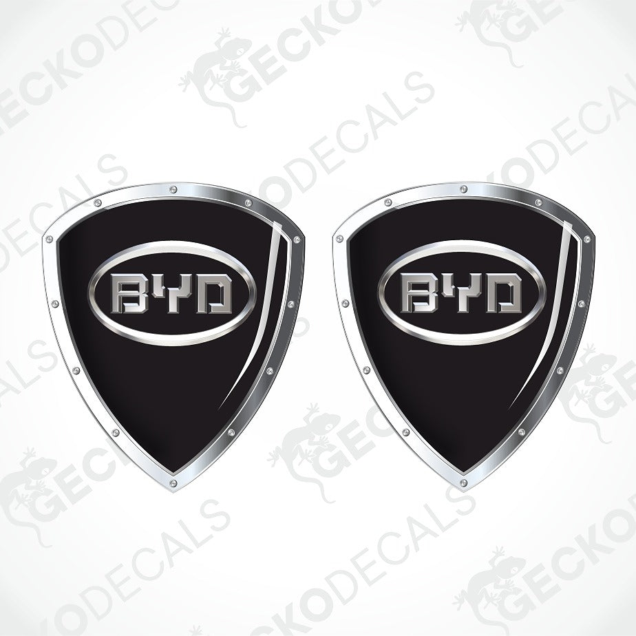 Two identical black shield-shaped decals with silver metallic borders and a central BYD logo, shown on a white background with diagonal watermarks.