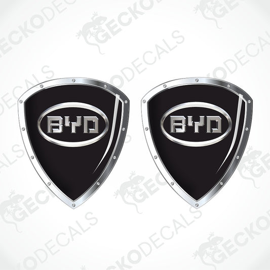 Two identical black shield-shaped decals with silver metallic borders and a central BYD logo, shown on a white background with diagonal watermarks.