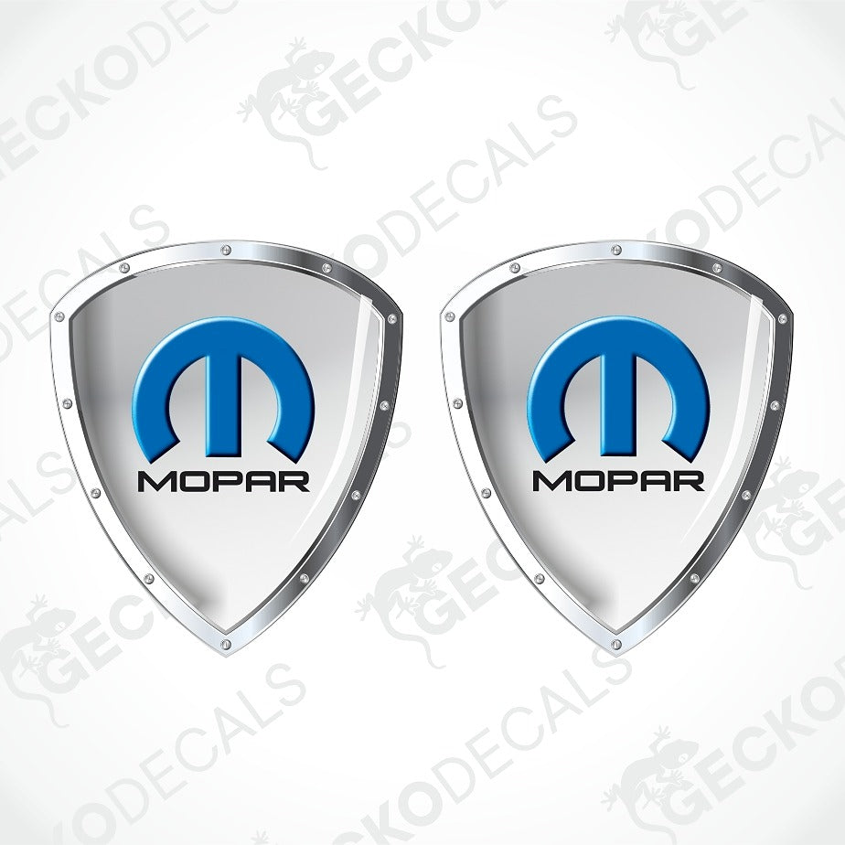 Two identical silver shield-shaped decals with the blue and black Mopar logo in the center, shown on a light gray background with diagonal watermark text.