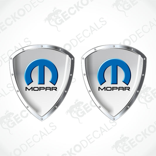 Two identical silver shield-shaped decals with the blue and black Mopar logo in the center, shown on a light gray background with diagonal watermark text.