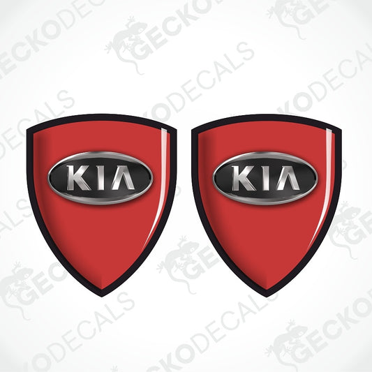 Two red shield-shaped Kia decal emblems with black borders and silver oval badges featuring the white KIA logo, shown on a light gray background with faint watermark text.