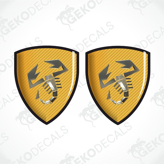 Two identical yellow carbon-fiber-textured shield decals with a black border and a stylized scorpion logo, shown on a white background with diagonal watermark text.
