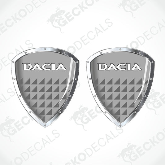 Two identical grey shield-shaped Dacia decals with silver borders and white lettering, shown on a light gray background with a faint watermark pattern.