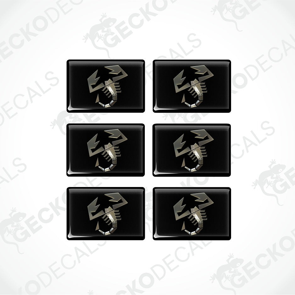Six glossy black rectangular decal stickers arranged in a 3x2 grid on a light gray background. Each sticker features a metallic silver scorpion graphic.