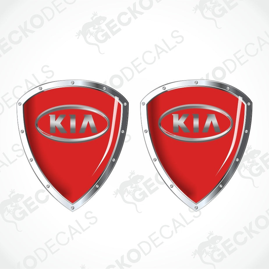 Two red shield-shaped KIA decal emblems with silver metallic borders and the KIA logo in the center, shown on a light gray background with faint GECKODECALS watermarks.