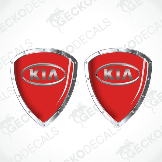 Two red shield-shaped KIA decal emblems with silver metallic borders and the KIA logo in the center, shown on a light gray background with faint GECKODECALS watermarks.