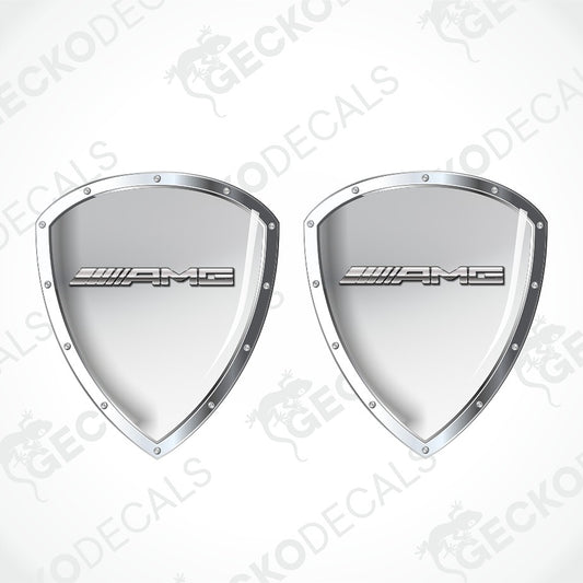 A pair of silver Mercedes-AMG shield-shaped decals with the AMG logo in the center, displayed on a light gray background with diagonal watermarks.
