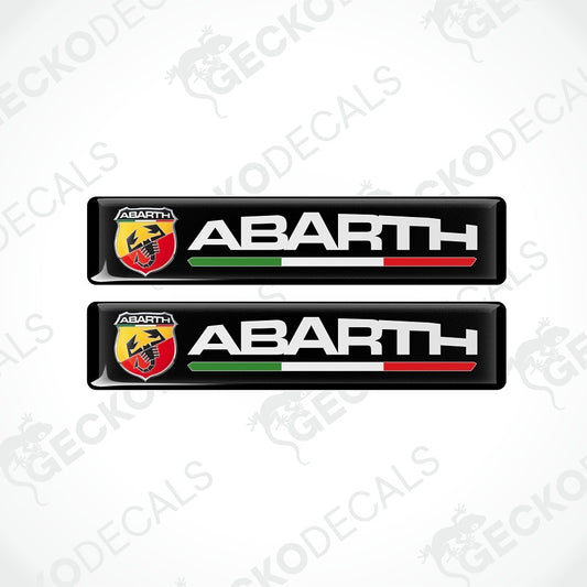 Two black Abarth car decal stickers on a light gray background with diagonal watermarks. Each sticker features the Abarth logo, the word 'ABARTH' in white, and a green, white, and red horizontal stripe.