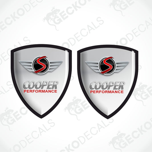 Two identical shield-shaped decal designs on a light gray background. Each shield has a black border, a silver-gray gradient center, a red and black winged 'S' logo, and the words 'COOPER PERFORMANCE' in gray and red.
