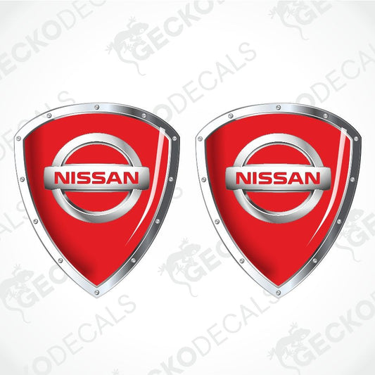 Two red Nissan shield-shaped decals with silver metallic borders and the Nissan logo in the center, shown on a light gray background with faint watermark text.