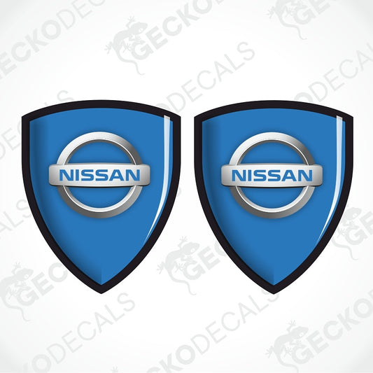Two blue Nissan shield-shaped decals with the Nissan logo in the center, shown on a light gray background with faint GECKODECALS watermarks.