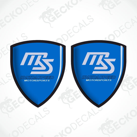 Two identical blue shield-shaped decals with black borders, featuring a white stylized 'MS' logo and the text 'MAVIDASPEED MOTORSPORTS' on a light gray background with faint diagonal watermarks.