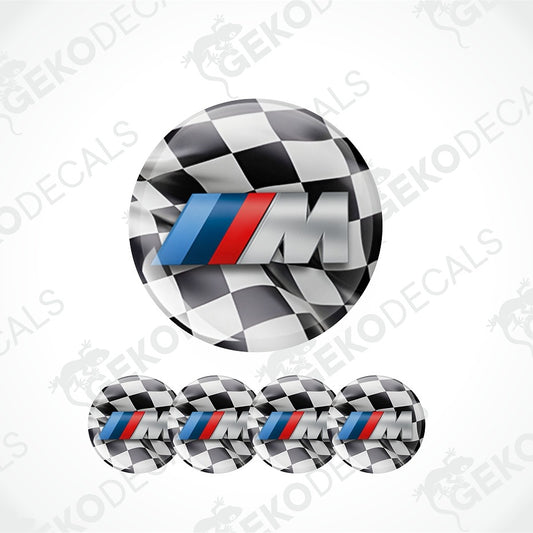 A set of circular decals featuring a black and white checkered pattern with a prominent silver 'M' logo accented by the classic blue and red stripes of the BMW M series. The main decal is shown large at the top, with four smaller versions aligned horizontally at the bottom against a white background with diagonal watermarks.