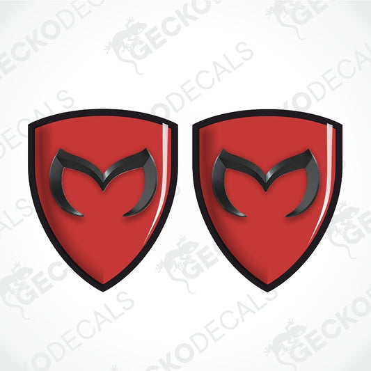 Two red shield-shaped decals with black borders and a black stylized 'M' emblem in the center, shown on a light gray background with diagonal watermark text.