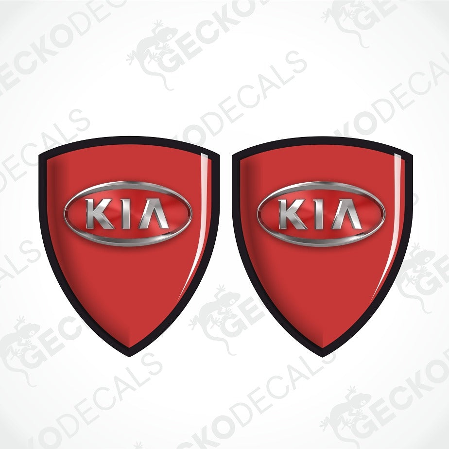 Two red shield-shaped Kia decal emblems with black borders and silver metallic Kia logos, shown on a white background with diagonal watermarks.