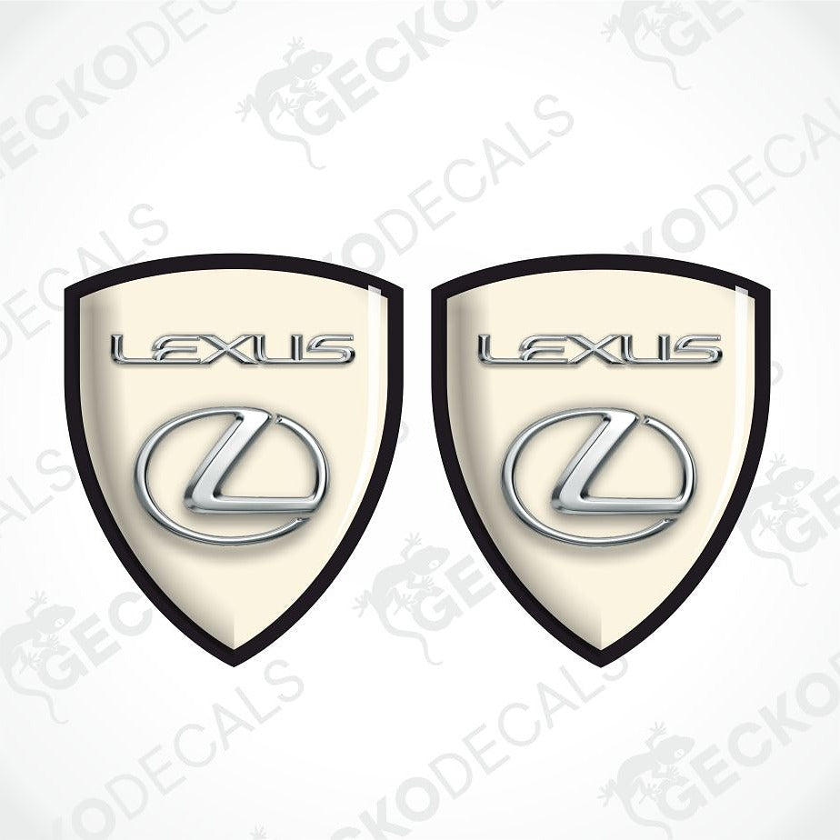 Two identical Lexus shield-shaped decals on a white background with diagonal watermarks. Each decal has a cream center, black border, silver Lexus wordmark, and silver Lexus logo.