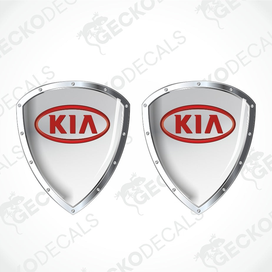 Two identical glossy shield-shaped car decals with silver borders and the red Kia logo in the center, shown on a light gray background with faint watermark text.