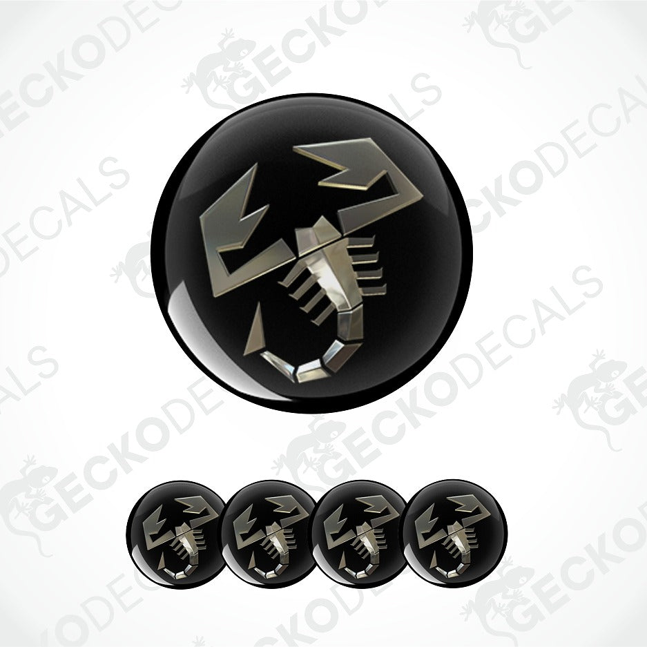 A glossy black circular decal or button featuring a stylized metallic silver scorpion symbol, shown with four smaller identical decals aligned horizontally below on a light gray background with faint GECKODECALS watermarks.