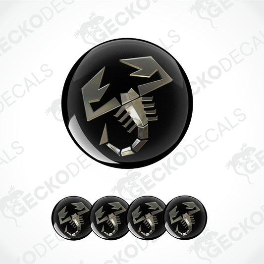 A glossy black circular decal or button featuring a stylized metallic silver scorpion symbol, shown with four smaller identical decals aligned horizontally below on a light gray background with faint GECKODECALS watermarks.