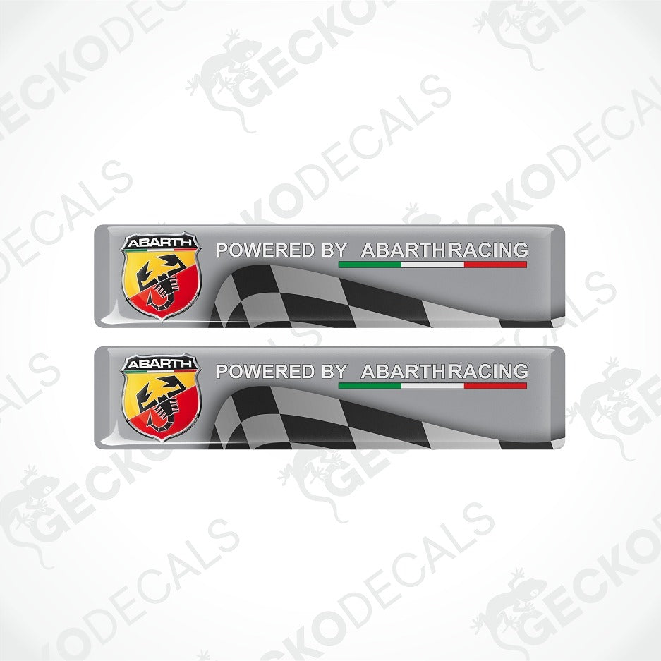 Two rectangular Abarth racing decal stickers shown on a light gray background. Each sticker is silver with a black-and-white checkered flag graphic, the text 'POWERED BY ABARTHRACING,' and the Abarth logo in red, yellow, black, and white.