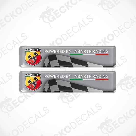 Two rectangular Abarth racing decal stickers shown on a light gray background. Each sticker is silver with a black-and-white checkered flag graphic, the text 'POWERED BY ABARTHRACING,' and the Abarth logo in red, yellow, black, and white.