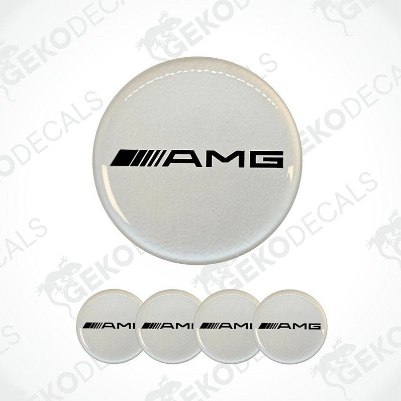 A set of four white vinyl stickers with the AMG (Alternate Mercedes-Benz) logo on them. The stickers are designed to be used on car wheel caps.